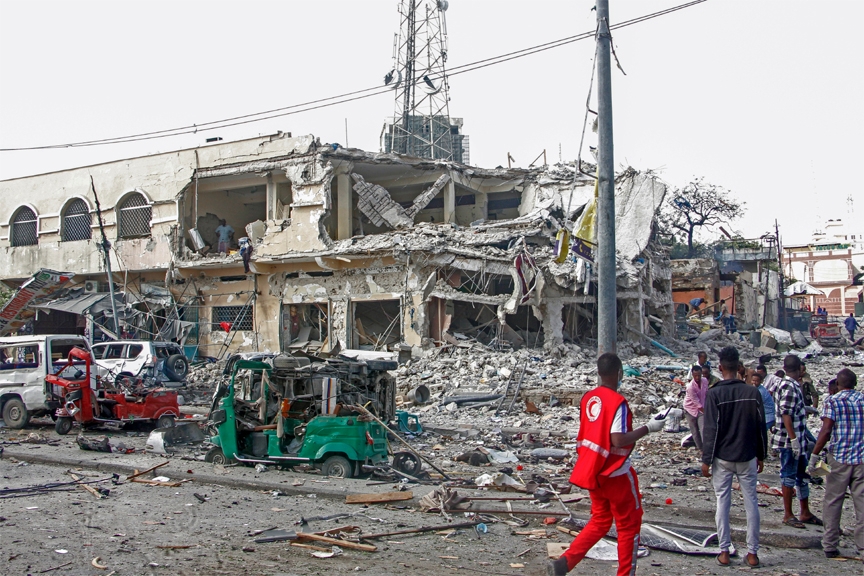 People observe a destroyed building and vehicles at the scene of a two car bombs attack in Mogadishu, Somalia, Saturday Oct. 29, 2022.