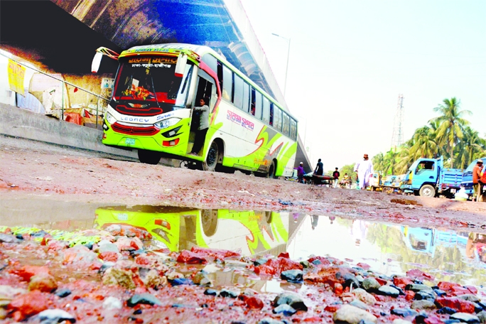Pedestrians as well as a bus move beside a road that is full of quagmire on Dhaka-Chattogram Highway on Wednesday.